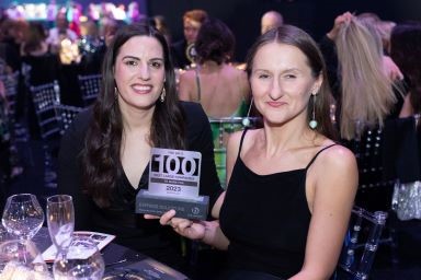 Two women sat at dinner table holding an award